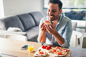 man seating having breakfast toast covered with tomatoes and eating it