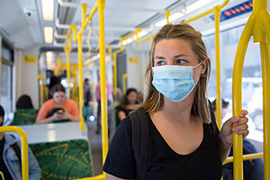 A woman wearing a facemask standing inside of a bus