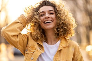 woman wearing a yellow jacket with blonde curly hair laughing out loud