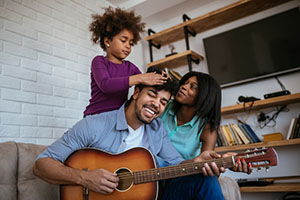 A man playing the guitar to a woman and small child