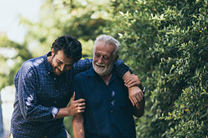 elderly father and middle age son walking with arms around each others shoulders